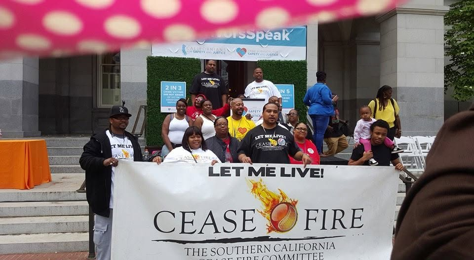 A crowd at a CEASE FIRE Southern California rally holding a banner that reads 'LET ME LIVE!' at the state capitol