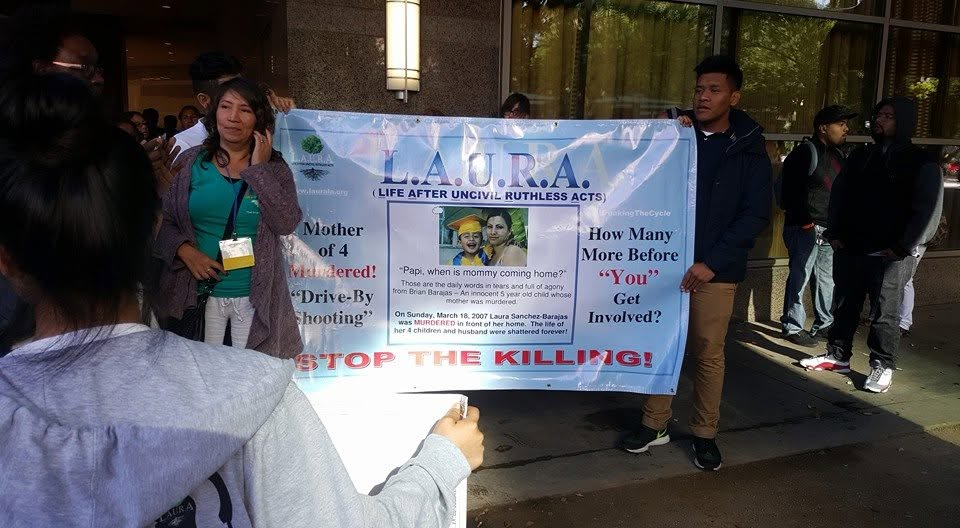 Advocates hold a L.A.U.R.A. banner reading STOP THE KILLING at a rally, honoring Laura Sanchez-Barajas and her four children